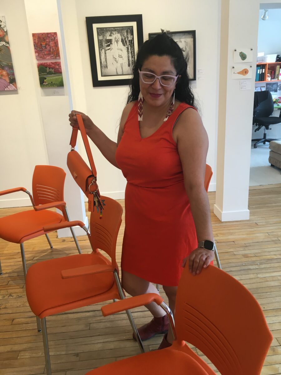 Adriana stands next to our new orange chairs wearing an orange dress and holding an orange handbag.