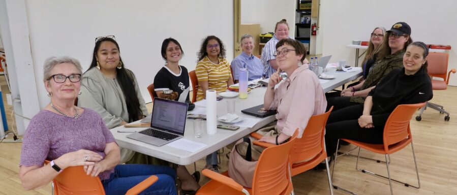 A group of people sit around a table, turned to look at the camera.