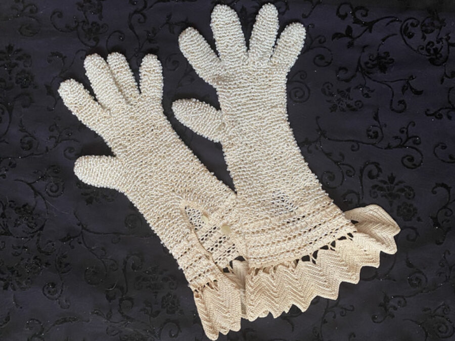 A pair of white beaded gloves on a black background