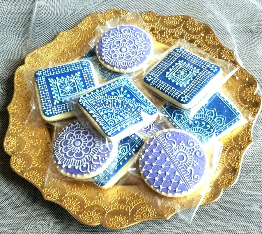 A plate of cookies with intricate designs made from white icing on top of blue icing.