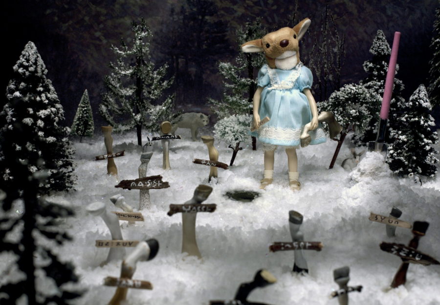 Photograph of a diorama of a girl with a deer head standing in a snowy cemetery where the crosses are made out of deer legs.
