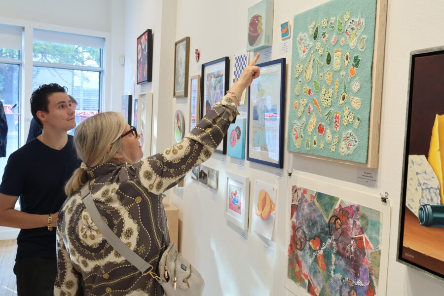 Two visitors to the 2023 MAWA members' show stand looking at the art. One points to an artwork on the wall.