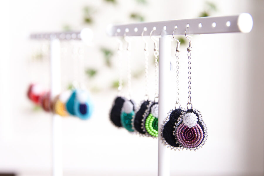 Many beaded earrings of different colours hang from a stand. They are all in the shape of little berries.