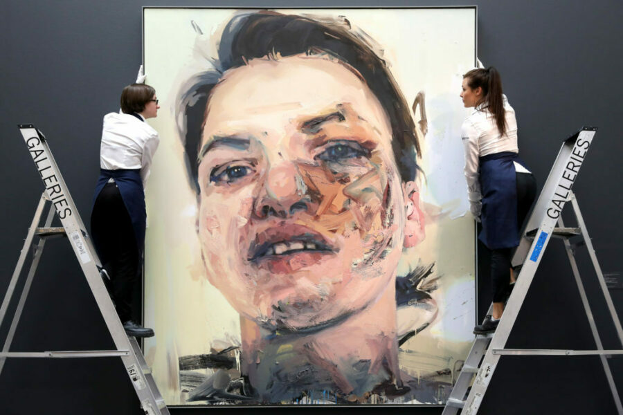 Two people on ladders adjust a large painting by Jenny Saville. The painting is a portrait rendered in a loose style.