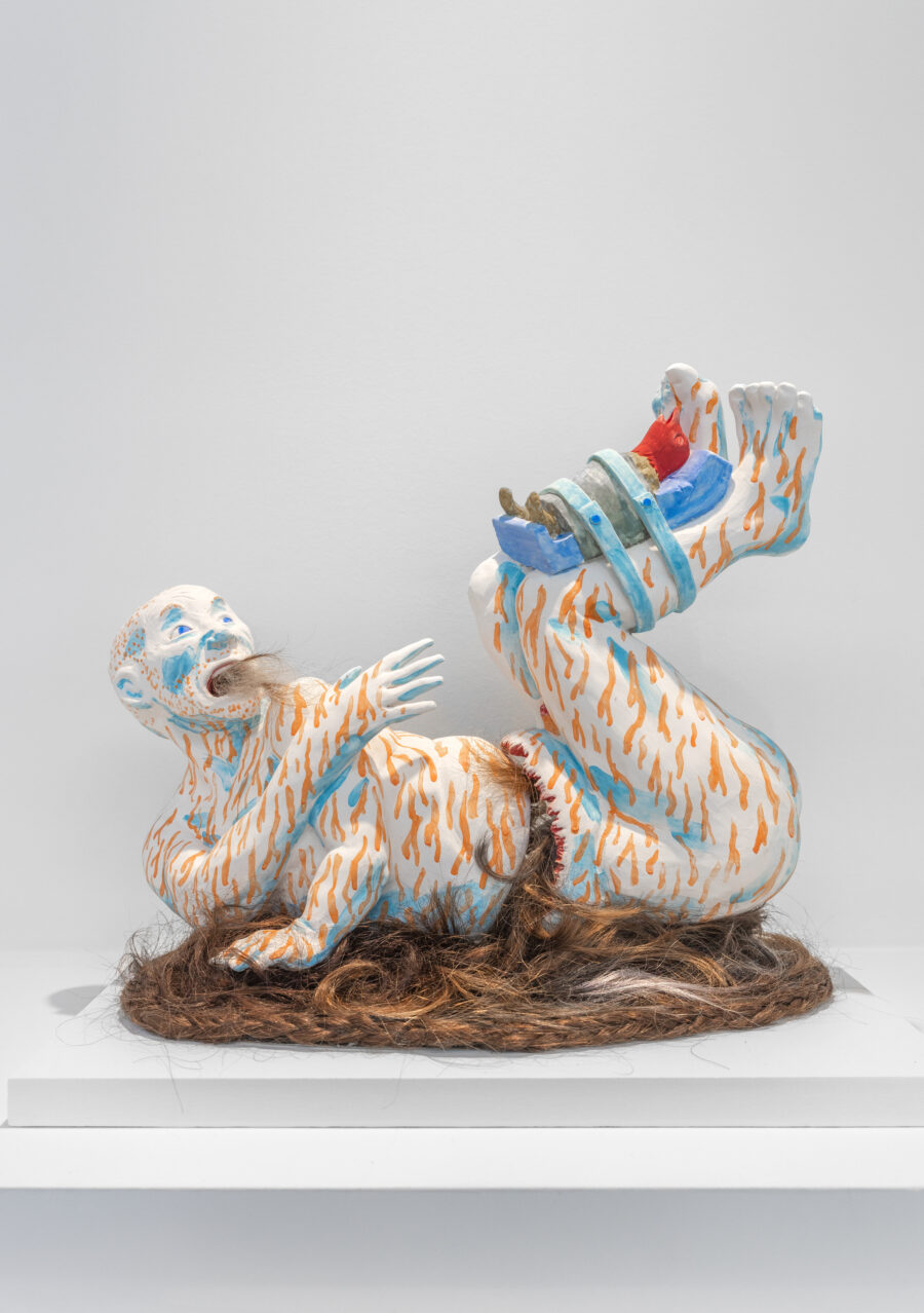 Ceramic sculpture by Lisa Walter depicting a person laying in a contorted position on human hair. Hair also comes out from their mouth. They are covered in bleeding pinpricks and have a bird strapped to a board around their legs.