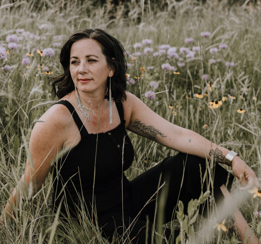 Photo of Shauna Fontaine sitting in a field with tall grass and flowers.
