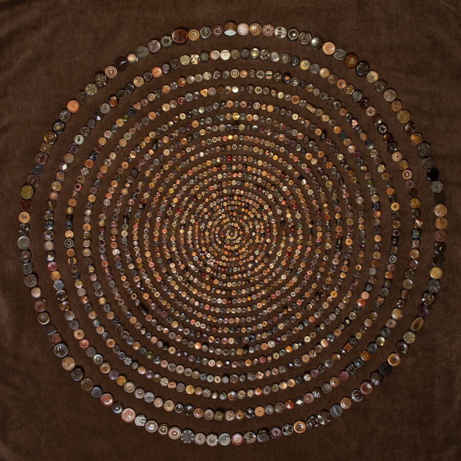 Buttons sewn onto a dark brown cloth in expanding circles like tree rings.