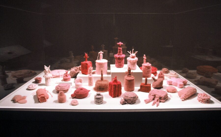 An installation of numerous knitted reproductions of various anti personnel mines in shades of pink on a white platform in a darkened gallery.