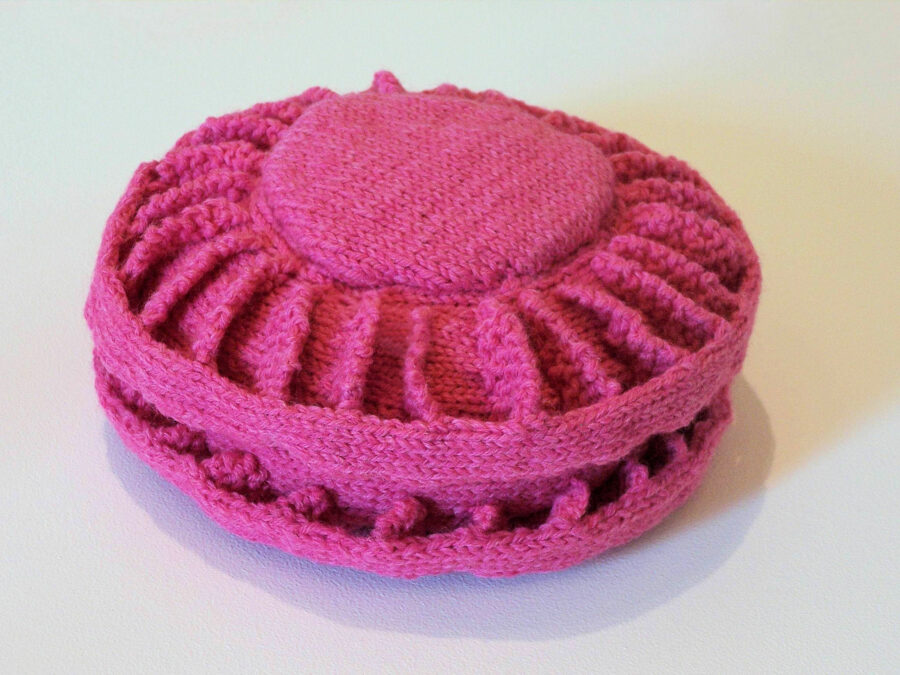 Pink knitted sculpture of a antipersonnel landmine.