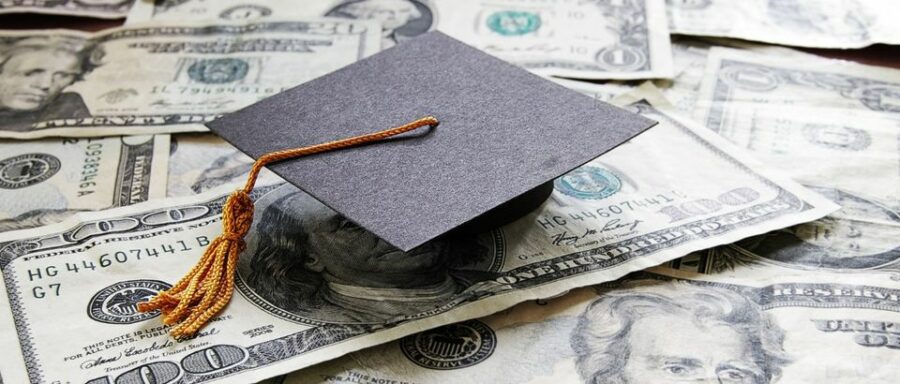 A graduation cap, mortarboard with yellow tassel, sits on $100 and $50 American bills.