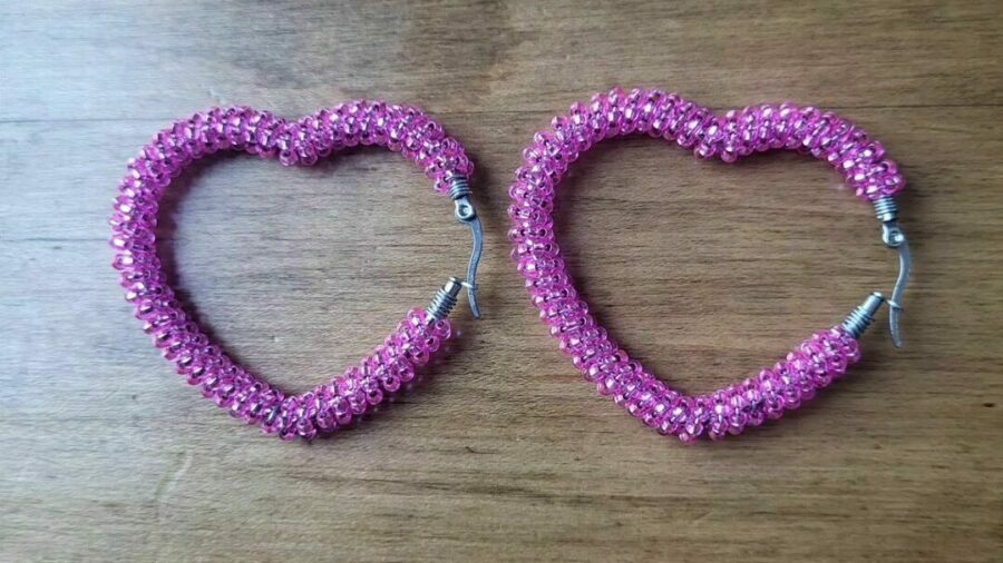 Beaded earrings using a wire hoop in the shape of a heart. Purple beads encircle the loop.