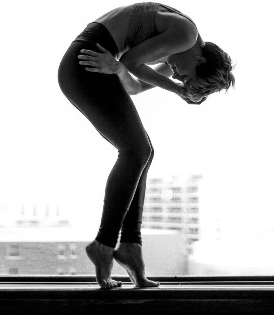 Black and white photo of Carol-Ann Bohrn silhouetted against a window. Bohrn is hunched over at the waist while standing on tiptoe.