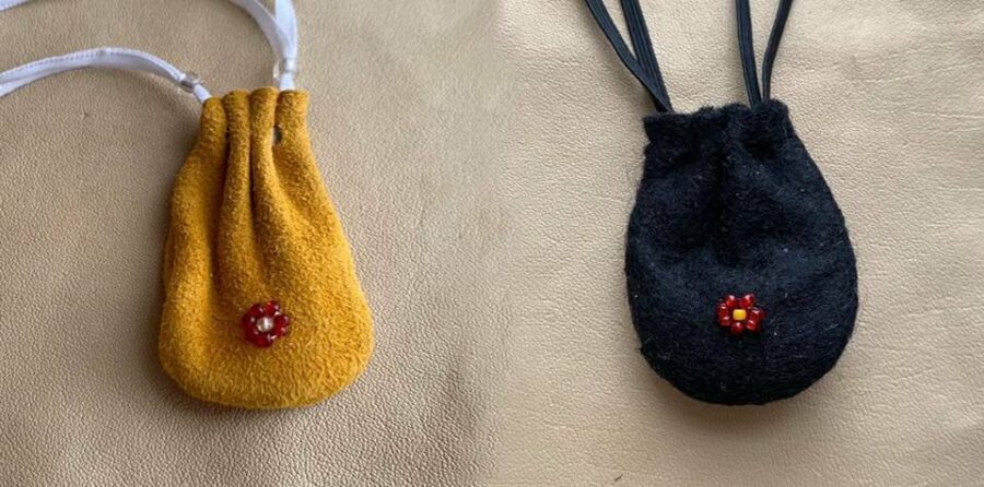 Two small drawstring pouches. One is made out of yellow leather and the other out of black felt. Each has a small beaded red rosette in the center.