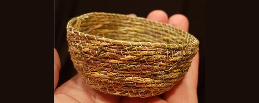 A small basket woven out of sweet grass sits in the palm of a hand.
