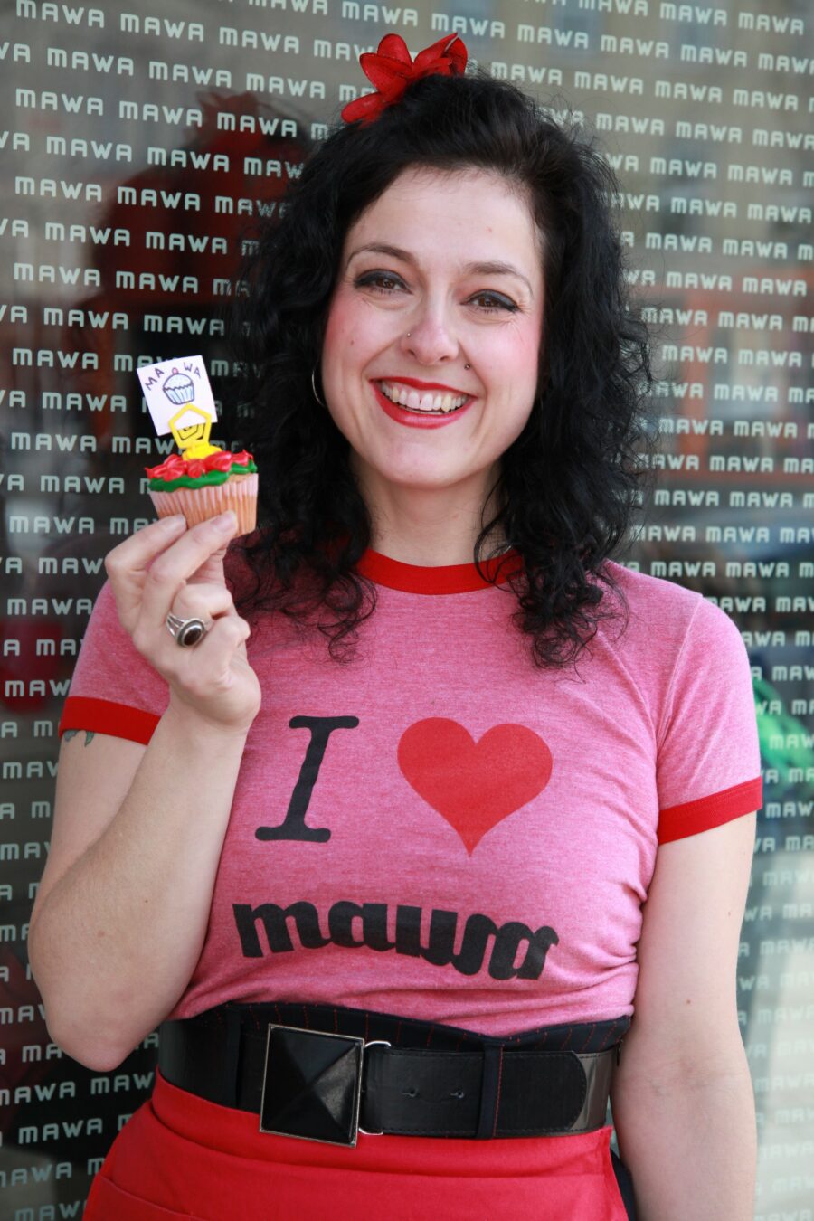 A smiling woman wears a pink t-shirt with the words I Heart MAWA on it.