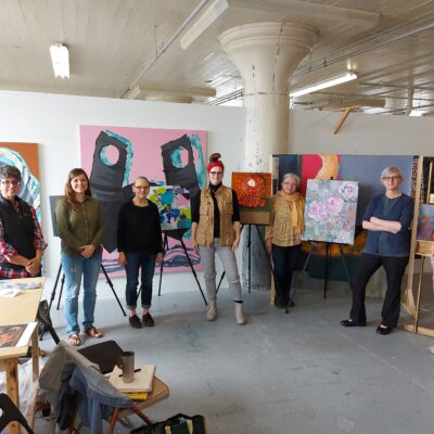 Seven people stand in a painter's studio.
