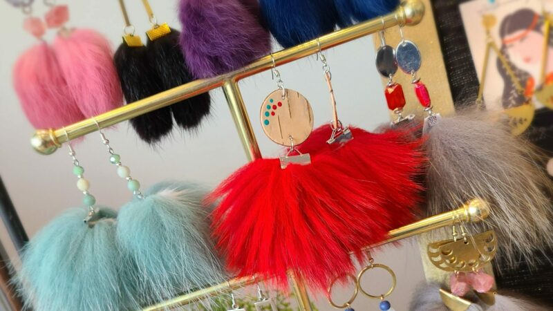 Three sets of earrings made from rabbit fur pom poms on a stand.