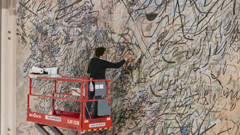 Painter Julie Mehretu stands on a large mechanical lift to work on a very largescale abstract painting.