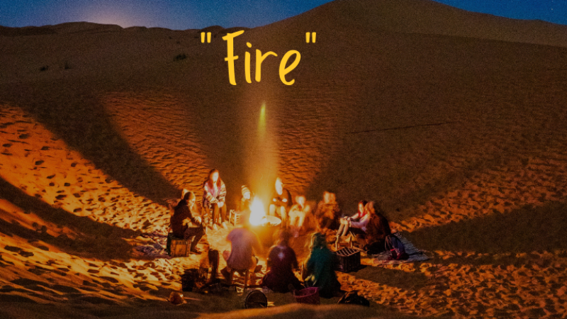 A group of people sit around an outdoor fire. Yellow text above them says Fire