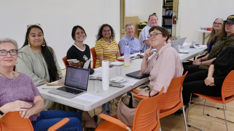 A group of people sit around a table, turned to look at the camera.