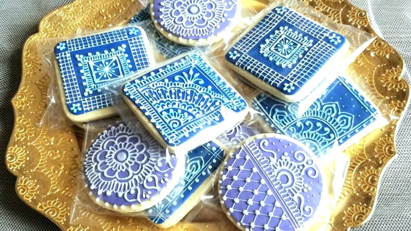 A plate of cookies with intricate designs made from white icing on top of blue icing.