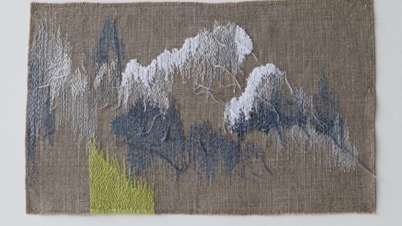 Abstract embroidery in white, grey and green thread on a dark beige fabric by Sonia Lofgren-Birch.