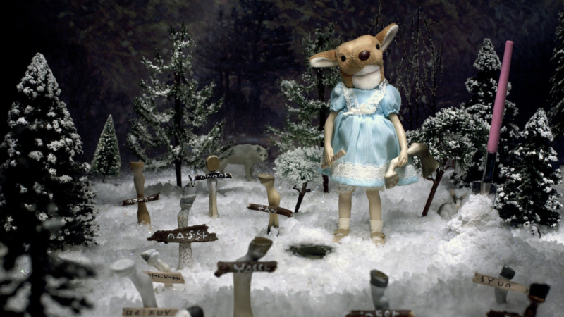 Photograph of a diorama of a girl with a deer head standing in a snowy cemetery where the crosses are made out of deer legs.