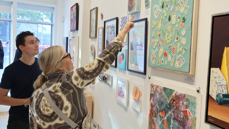 Two visitors to the 2023 MAWA members' show stand looking at the art. One points to an artwork on the wall.