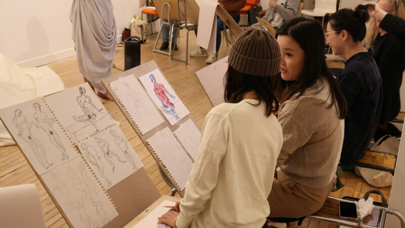People sit on drawing horses. Some of their sketches are visible.