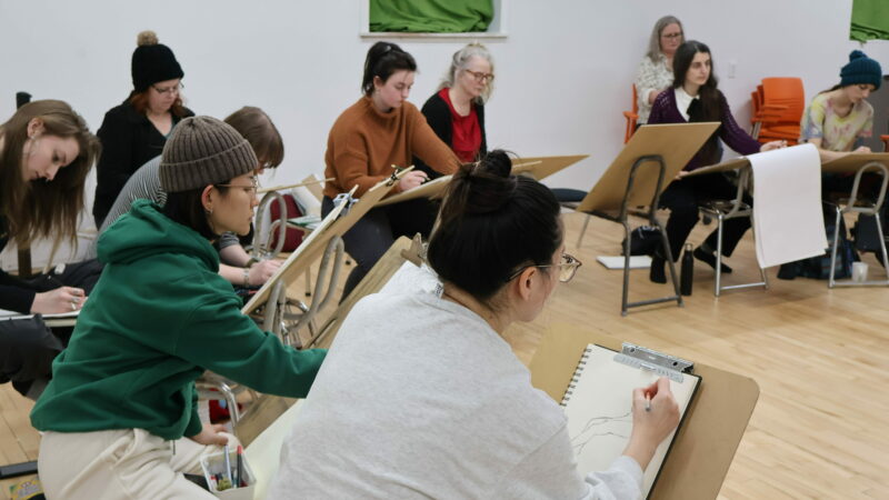A group of people sit at drawing horses sketching.