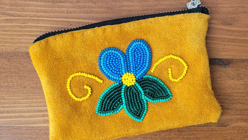 A small rectangular pouch with a zipper. Made out of hide with a blue flower beaded design.