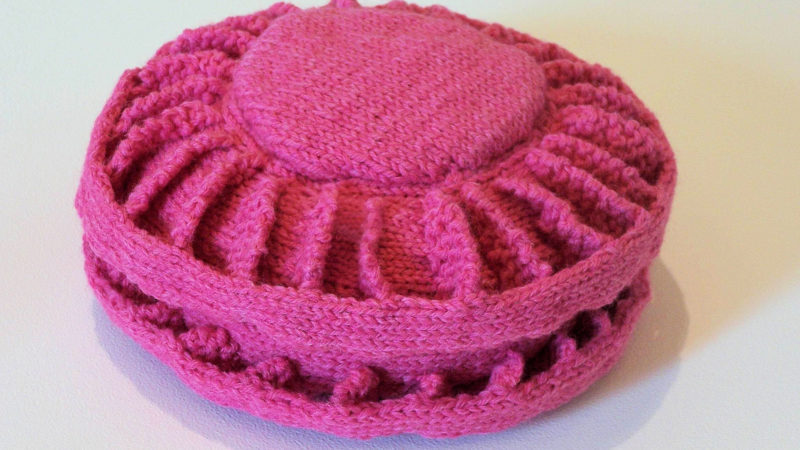 Pink knitted sculpture of a antipersonnel landmine.