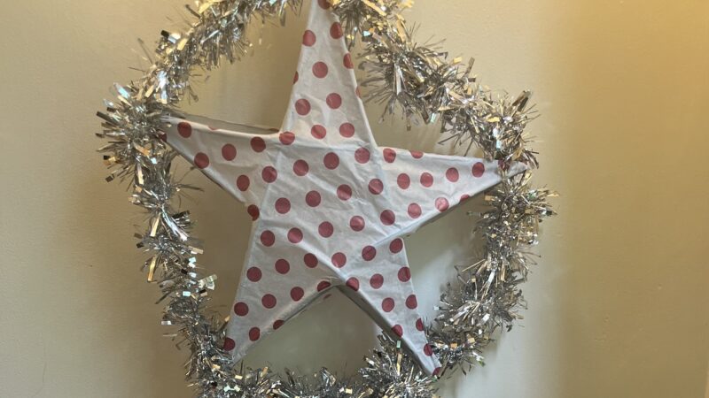 A decoration made out of paper and garlands that features a star shape in a circle with streamers hanging below.