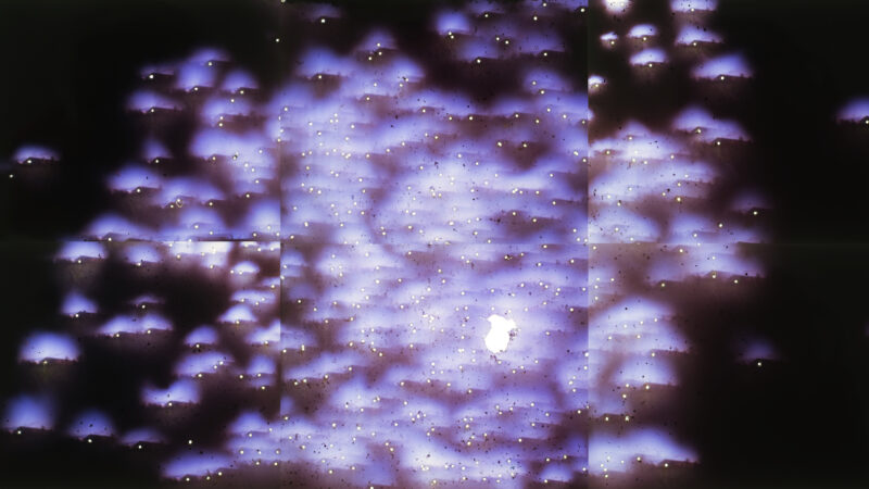 Artwork by Estelle Chaigne of many points of light with purplish auras exploding across a black background.