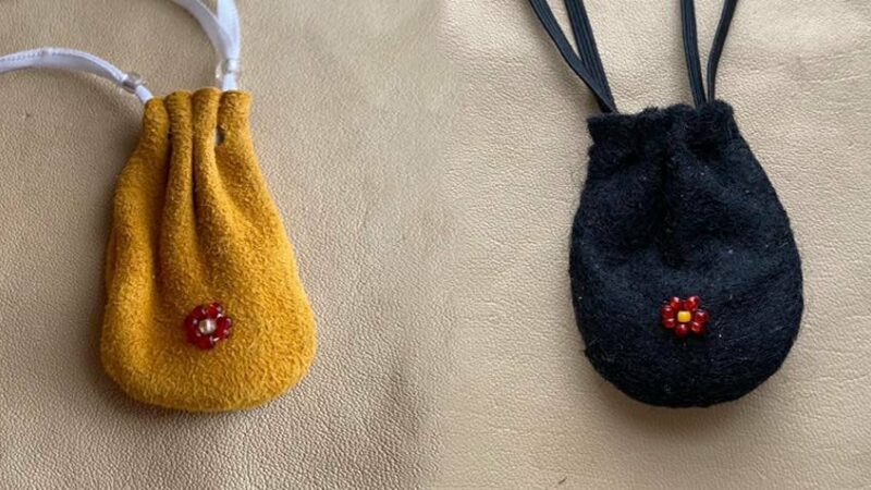 Two small drawstring pouches. One is made out of yellow leather and the other out of black felt. Each has a small beaded red rosette in the center.