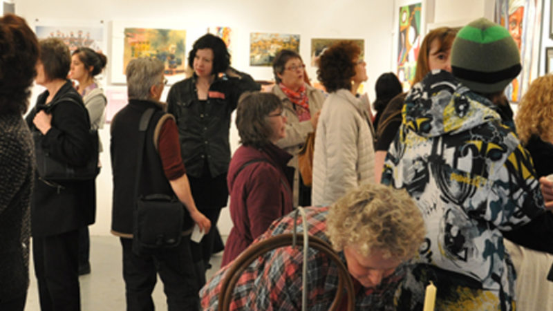 A group of people looking at artwork on the walls of the MAWA space.