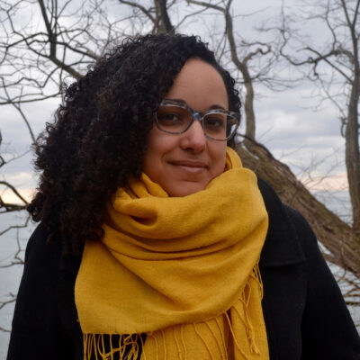Headshot of Erika DeFreitas standing outdoors wearing a yellow scarf and dark jacket.
