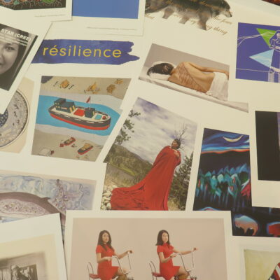8.5 x 11 inch art reproductions from the boxed set of Resilience: 50 Indigenous Art Cards and Teaching Guide are scattered across a table.